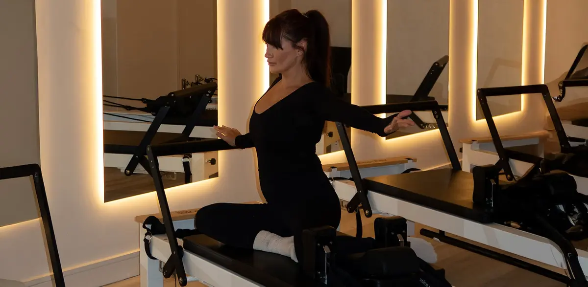A client kneeling on a reformer, holding the straps, in the warmly lit studio