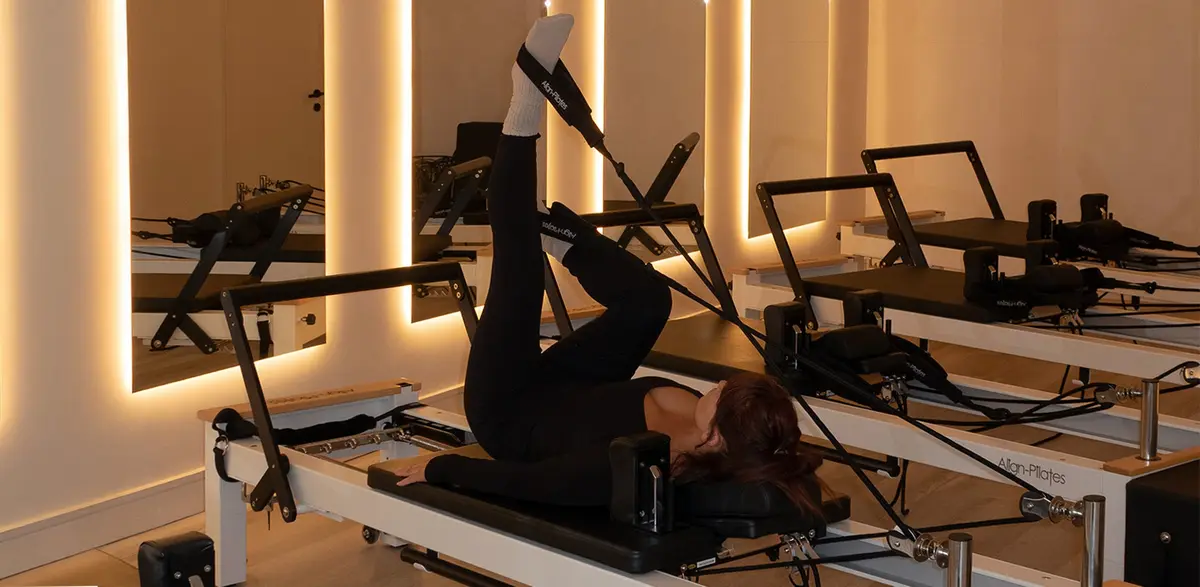 A client lying on a reformer with both legs raised in the straps