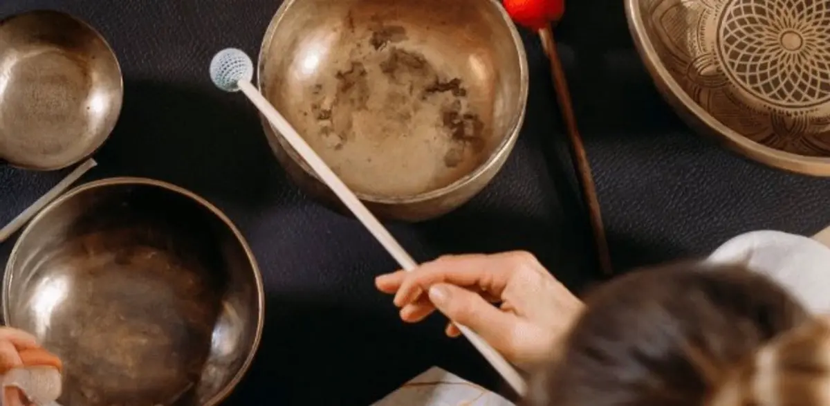 Hands playing brass singing bowls during a sound bath